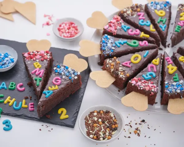 Schokoladenkuchenstücke mit bunten Buchstaben und Zahlen, die "ABC SCHULE" ergeben. Ein perfekter Kuchen zur Einschulung!