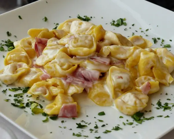 Tortellini panna e prosciutto, un classico piatto italiano, serviti su un piatto bianco con prezzemolo tritato.