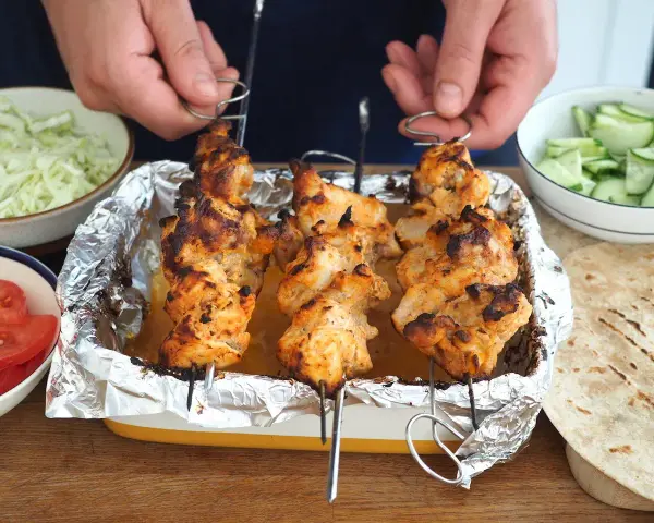 Domowy kebab: grillowane szaszłyki z kurczaka w tacce, obok miseczki z warzywami i tortille.