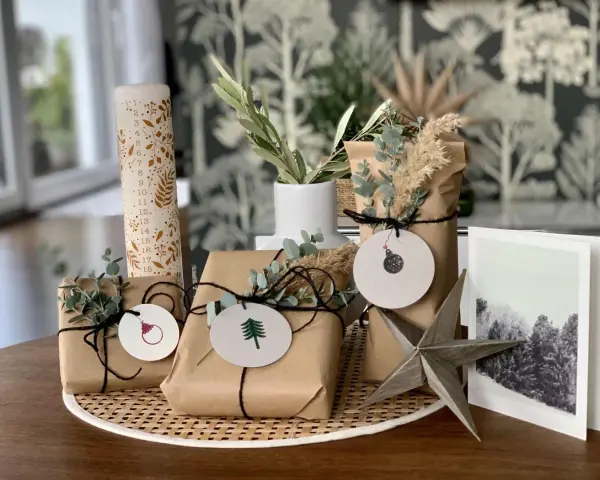 Schöne Geschenk verpacken Ideen: Geschenke in braunes Papier, mit Zweigen und Anhängern dekoriert, neben einer Adventskerze und einer Weihnachtskarte.