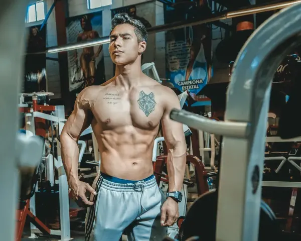 Muskulös man med tatueringar i gym. Han har en imponerande fysik, ett resultat av hårt arbete och att **deffa mat**.