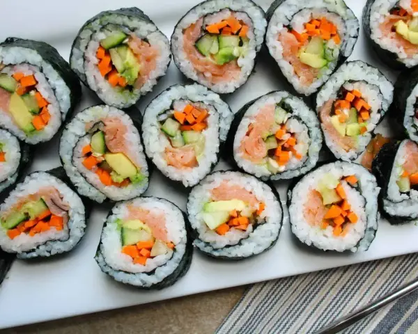 Ułożone na talerzu rolki sushi z łososiem, awokado, ogórkiem i marchewką. Widać, co do sushi do środka, czyli świeże składniki.