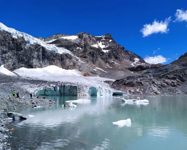 Un lago glaciale riflette montagne imponenti e il ghiacciaio Fellaria, con iceberg che galleggiano sull'acqua turchese.