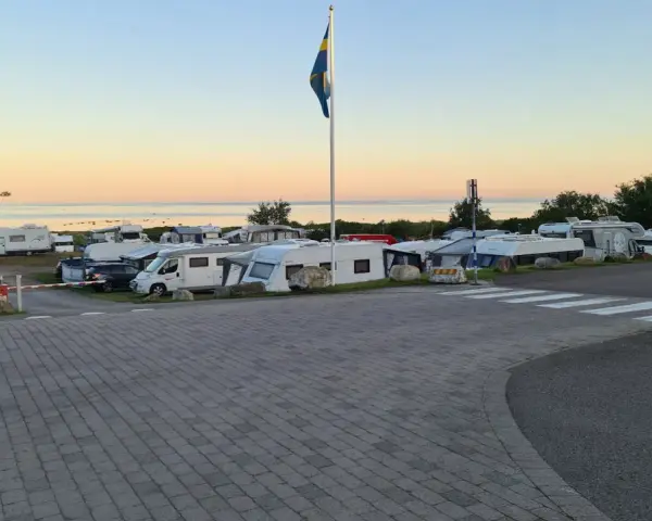 Solnedgång över Lerbergets camping med husbilar och husvagnar uppställda. En svensk flagga vajar i vinden.