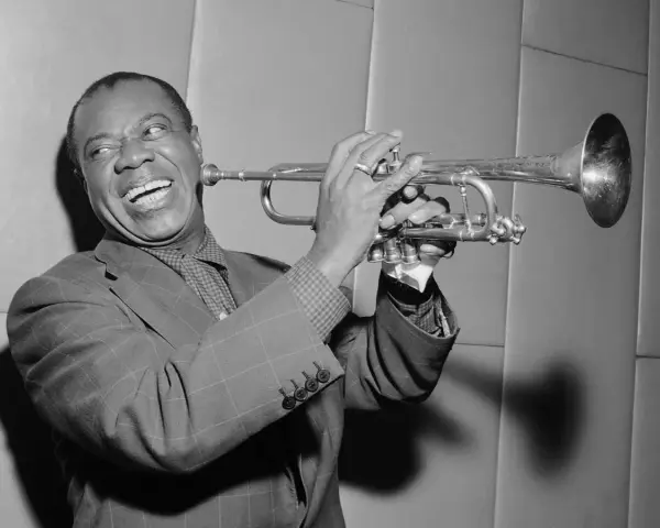 Louis Armstrong, znany jako "Satchmo", gra na trąbce z charakterystycznym uśmiechem.