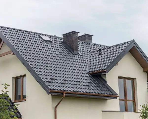 Nowoczesne opierzenie dachu z ciemnej blachodachówki, z dwoma kominami i okapem.