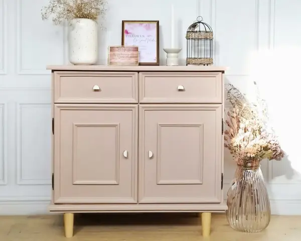 Meuble ancien repeint en rose poudré, avec deux tiroirs et deux portes. Décoré de fleurs séchées et d'une cage à oiseaux.