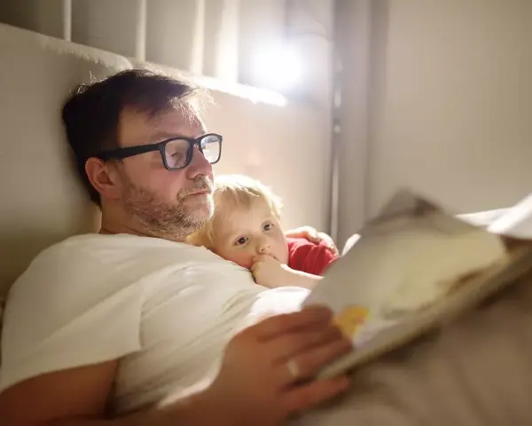 Vater im Elternzeit, 1 Monat alt, liest seinem Kind im Bett eine Geschichte vor.