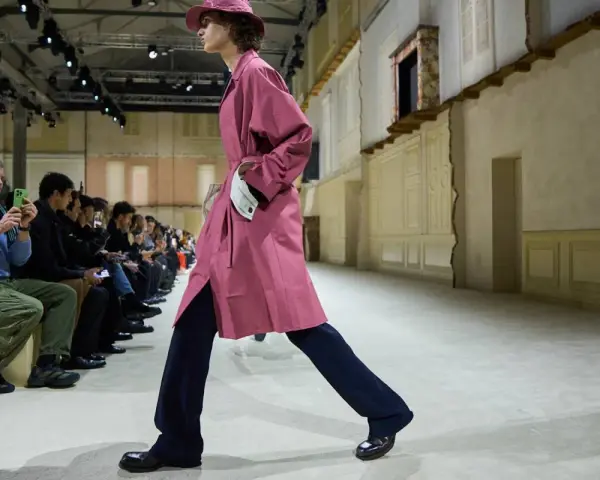 Modello sfila con trench rosa e pantaloni blu, un esempio di moderno stile uomo.