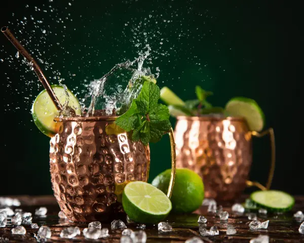 Dwa miedziane kubki z Moscow Mule i London Mule, ozdobione limonką i miętą, z bryzgami wody i lodem.