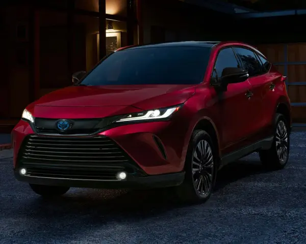 Elegancka, czerwona Toyota Venza z nowoczesnymi światłami LED stoi przed domem o zmierzchu.