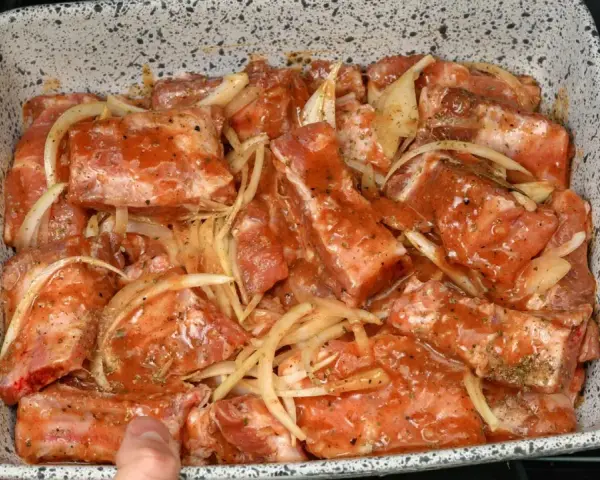 Babcine żeberka w sosie własnym, gotowe do pieczenia. Mięso w sosie z cebulą, przyprawione ziołami, w naczyniu żaroodpornym.
