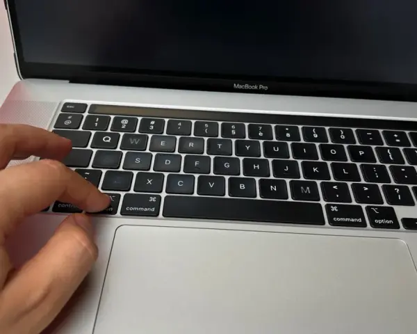 Dłoń naciska klawisz "command" na klawiaturze MacBooka, przygotowując się do instalacji drukarki.