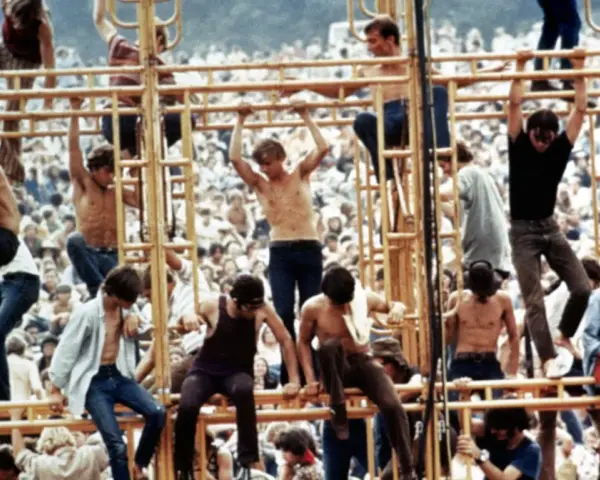 Tłum ludzi na festiwalu, niektórzy wspinają się na konstrukcję. To właśnie woodstock co to za wydarzenie?