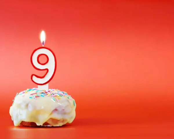 En söt donut med vit glasyr och strössel, toppad med en brinnande ljusformad siffra nio. Perfekt för ett kalas för en 9-årig kille!