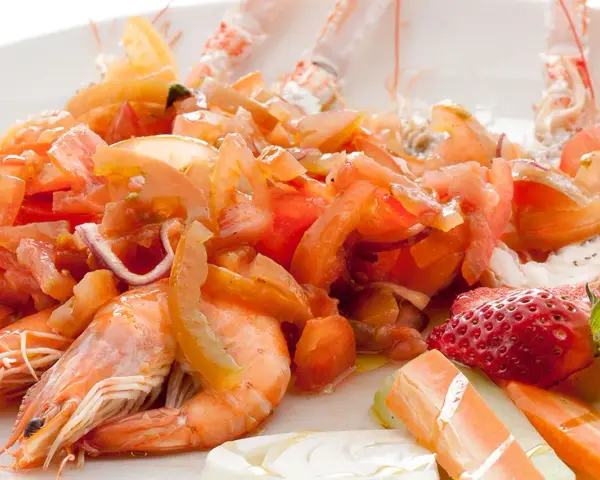 Scampi alla catalana: gamberi succulenti con pomodori freschi, cipolla rossa e una fragola decorativa. Un piatto colorato e invitante.