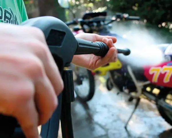 Mani che impugnano un'idropulitrice per pulire una moto da cross. Un modo efficace per capire come lucidare la moto.