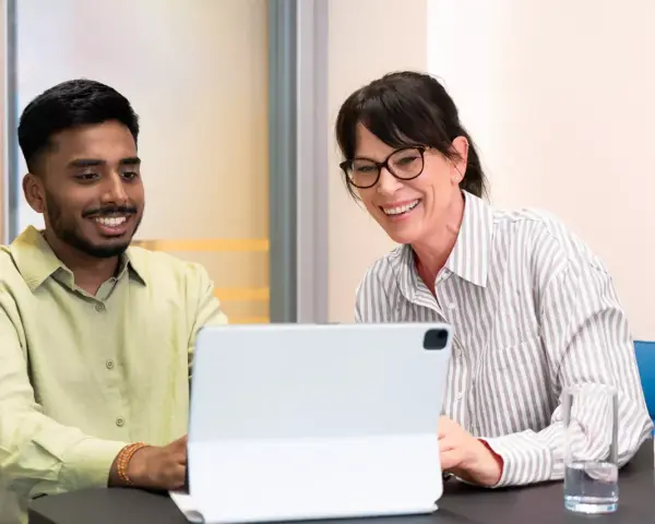 Ein junger Mann und eine Frau lachen über den Bildschirm eines Tablets. Sie sind bei einem Praktikum Studium und scheinen eine gute Zeit zu haben.