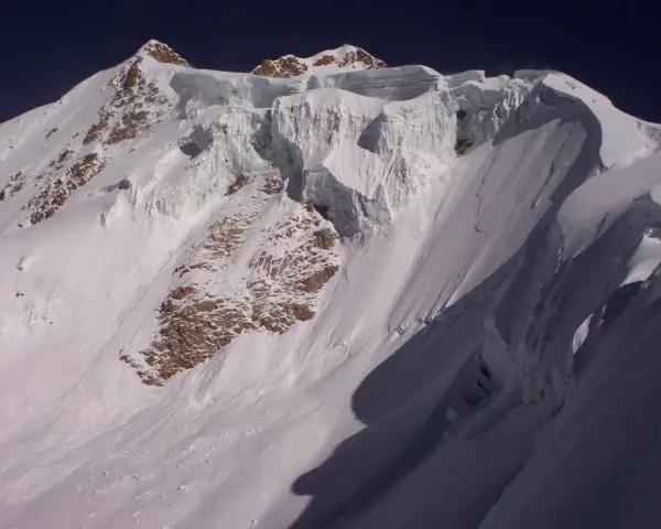 Schneebedeckte Gipfel des Huayna Potosí, mit steilen Eiswänden und felsigen Hängen unter einem tiefblauen Himmel.