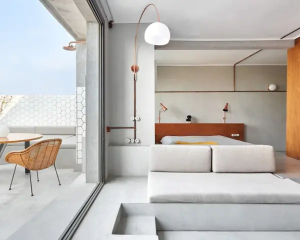 Habitación con diseño industrial, cama baja, sofá de lino y terraza con ducha exterior.