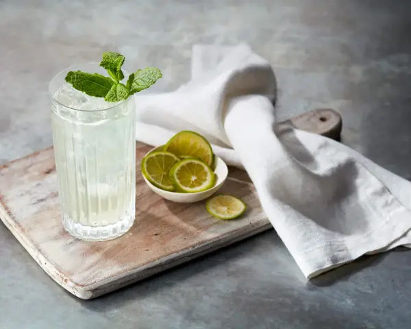 Orzeźwiający mojito z ginem, udekorowany miętą i podany z plasterkami limonki na drewnianej desce.