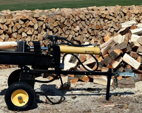 Czarna piło łuparka z żółtym cylindrem hydraulicznym stoi obok stosów drewna opałowego.