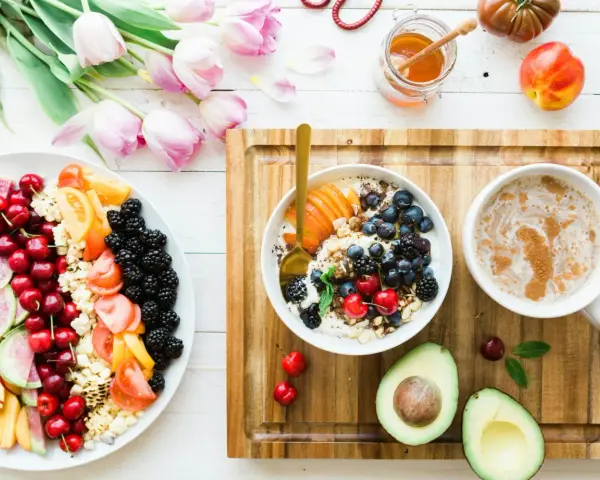 Un bol de yaourt aux fruits rouges, myrtilles et amandes, un plateau de fruits frais, un avocat et une tasse de café. Un repas sain, un aliment anti inflammatoire.