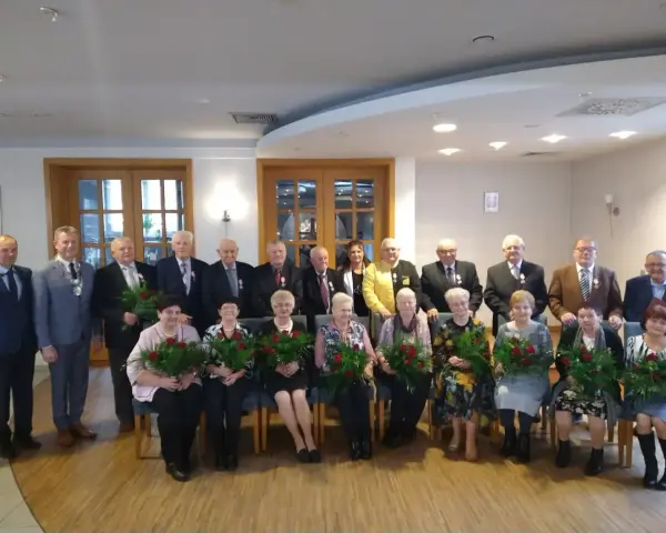 Grupa osób świętuje 50 rocznicę ślubu. Wszyscy otrzymują róże i medale.