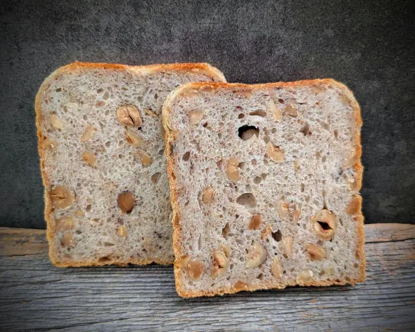 Zwei Scheiben salzarmes Brot mit Nüssen liegen auf Holz.