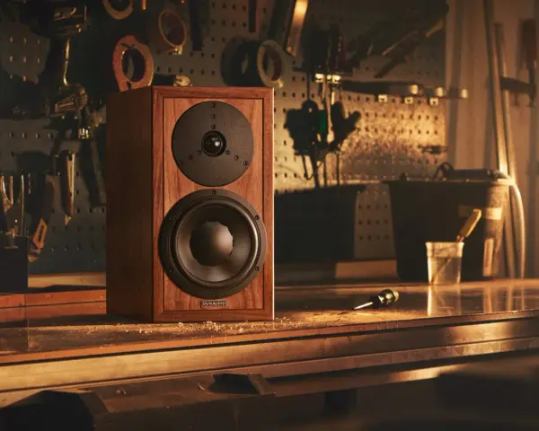 Głośnik Dynaudio Special 25 w drewnianej obudowie, stojący na stole w warsztacie, otoczony narzędziami.