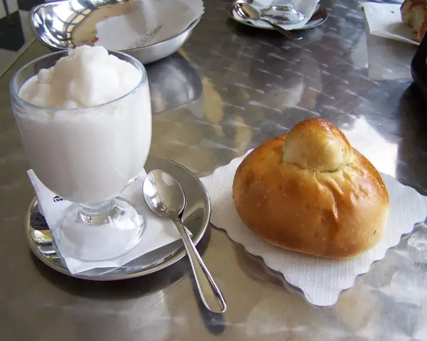 Un bicchiere di granita bianca e un soffice brioche col tuppo su un tavolo metallico.