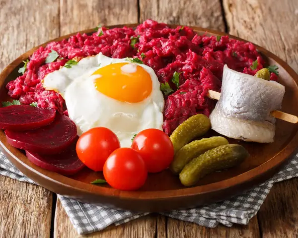 Labskaus: was ist das? Ein deftiges Gericht mit Roter Bete, Kartoffeln, Corned Beef, Spiegelei, Rollmops und Gewürzgurken.