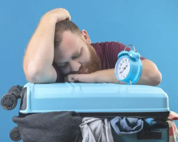 Zmęczony podróżnik śpi na walizce obok budzika. Czy to jetlag?