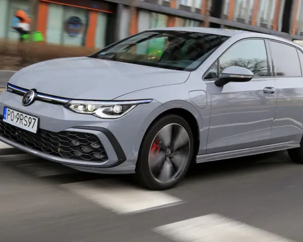 Szary Volkswagen Golf GTE porusza się po miejskiej drodze, z rozmytym tłem budynków i przechodniów.