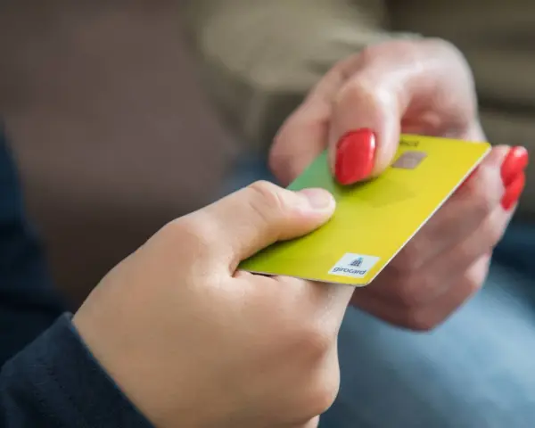 Eine Hand gibt einer anderen eine gelbe Girocard. Dies könnte die erste kinder debitkarte sein, die ein Kind erhält.