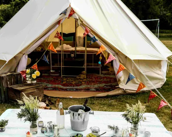 Idealne miejsce na glamping: namiot typu bell z kolorowymi chorągiewkami, stół z winem i kwiatami.