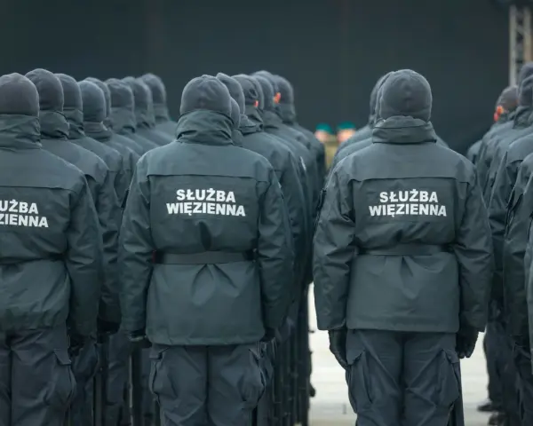 Grupa funkcjonariuszy Służby Więziennej w mundurach, widok od tyłu.