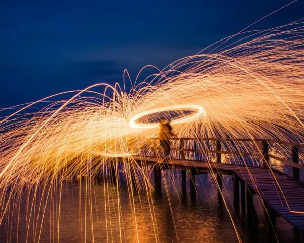 Une personne sur un pont crée une **light painting photo** spectaculaire avec des traînées de feu dans le ciel nocturne.