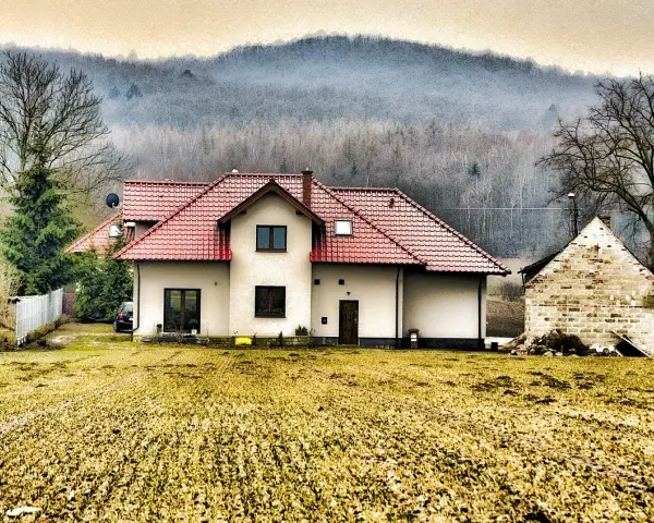 Dom z czerwonym dachem i polem przed nim. Rodzinna historia o przepisaniu domu na jedno dziecko bez zgody drugiego.