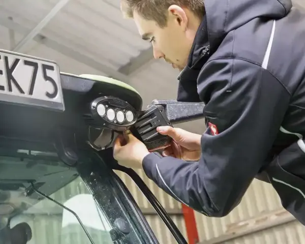 Mężczyzna dokonuje wymiany żarówki w lampie roboczej pojazdu.