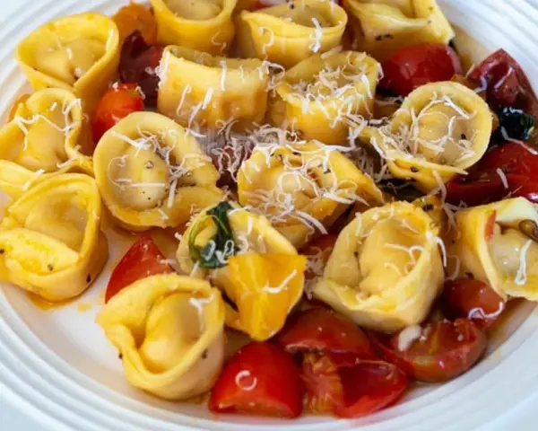 Pyszne tortellini z pomidorkami i parmezanem na białym talerzu. Idealne danie, czy ravioli czy tortellini?