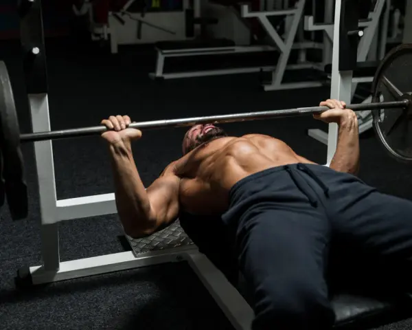 Man med skägg och synliga muskler utför bänkpress som en del av sitt starting strength program.