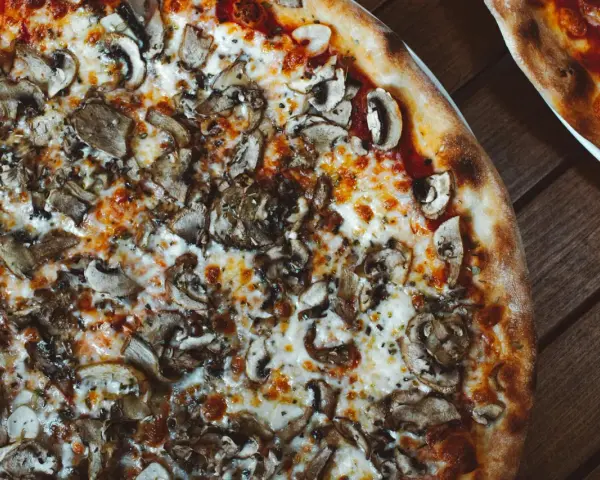 Pyszna pizza wegetariańska z pieczarkami i ciągnącym się serem, idealna na wspólny wieczór.