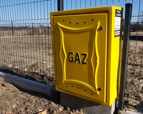 Żółta skrzynka gazowa z napisem "GAZ" przy ogrodzeniu. Zastanawiasz się, ile kosztuje przyłącze gazu?