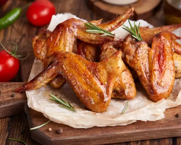 Alette di pollo dorate e succulente, cotte alla perfezione nella friggitrice ad aria, servite su carta forno con rosmarino, pomodorini e peperoncino.