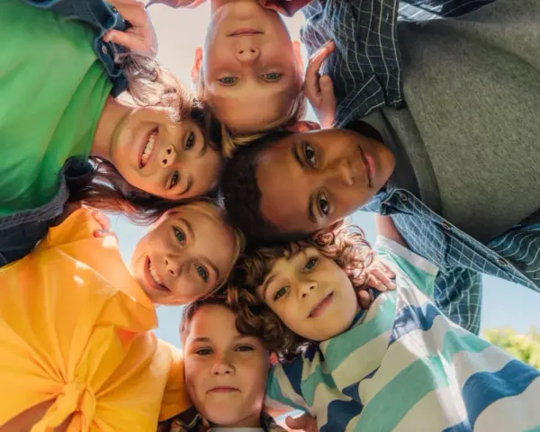 Un groupe d'enfants souriants forme un cercle, leurs visages se rejoignant au centre. Leurs regards joyeux et leurs expressions témoignent d'un bel encadrement d'enfants.