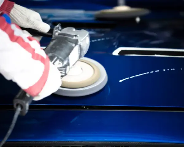 A gloved hand uses a buffer to polish a shiny blue car hood, demonstrating how to polish a car with a buffer for a flawless finish.