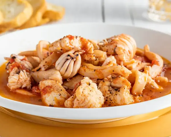 Un invitante piatto di zuppa di pesce, ricco di calamari, gamberi e pesce bianco, servito con crostini dorati.