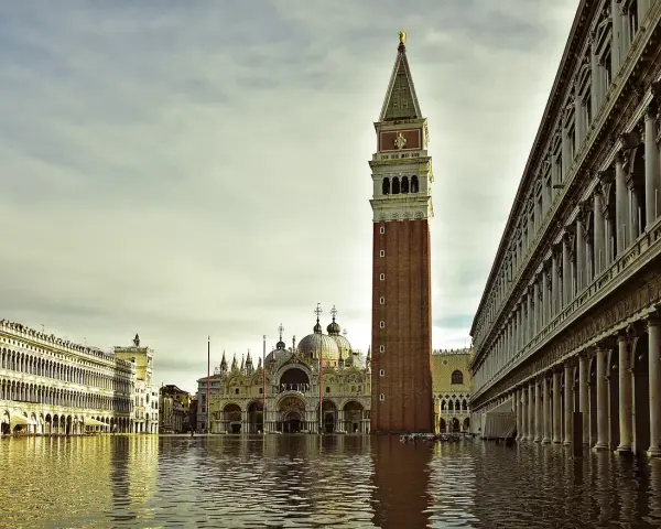 La maestosa torre di Piazza San Marco si erge sull'acqua alta, riflettendosi nel canale che lambisce i palazzi storici.