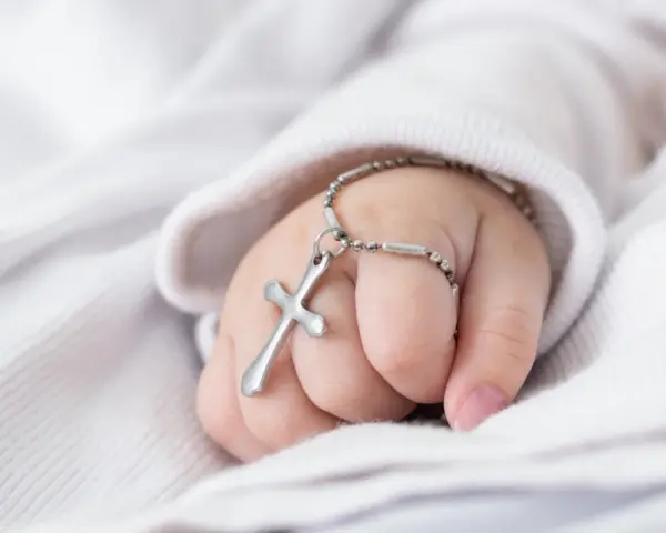Dziecięca dłoń z krzyżykiem na bransoletce, symbol błogosławieństwa podczas chrzcin dziecka.